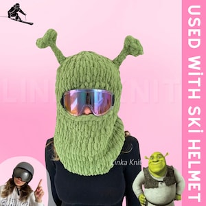 May include: Green knitted ski mask with a large, green, alien-like head and two long ears. The mask has a pair of ski goggles with a rainbow iridescent lens. The text "USED WITH SKI HELMET" is in white letters on a pink background.