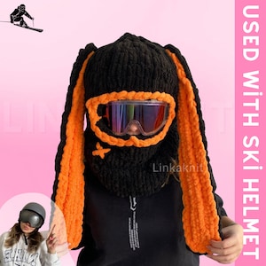 May include: Black knitted ski mask with orange ear flaps and a black ski goggle. The text "Linkaknit" is visible on the mask.