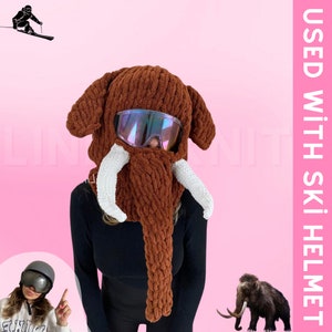 May include: A brown knitted ski mask shaped like a mammoth with white tusks and a pair of iridescent ski goggles. The text "USED WITH SKI HELMET" is visible in the background.