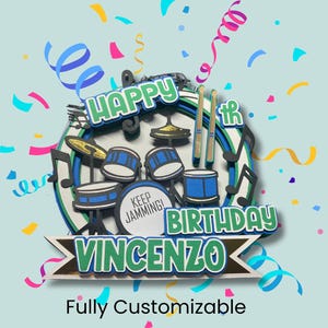 May include: A layered cake topper with a drum set design. The topper features the words "Happy Birthday Vincenzo" in green and white, with musical notes and drumsticks. The words "Keep Jamming!" are also included. The background is light blue with colorful confetti.