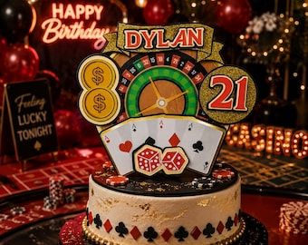 May include: A casino-themed cake topper featuring a gold banner with the name DYLAN, a roulette wheel, two gold dollar sign coins, the number 21, four playing cards showing aces, and two red dice. The topper sits on a white cake with gold flakes.