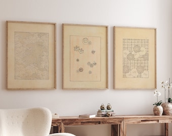 Puede incluir: Tres impresiones enmarcadas con diseños de inspiración japonesa cuelgan de una pared blanca sobre una mesa de madera con un sillón blanco. Las impresiones presentan patrones abstractos de olas, flores y formas geométricas. La mesa está decorada con un jarrón de flores blancas, una pila de libros y dos pequeños adornos de metal.