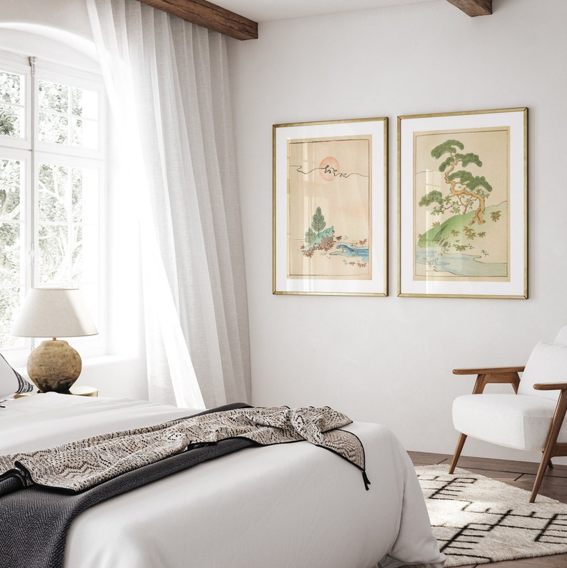 May include: Two framed Japanese-style prints of landscapes with trees and water. The prints are in gold frames and hang on a white wall.