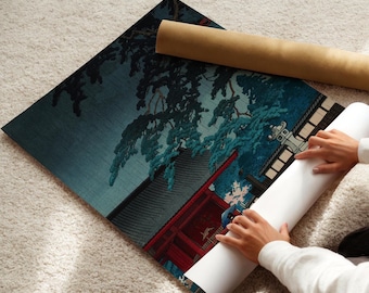 Può includere: Una persona sta arrotolando una stampa giapponese in stile blu e rosso di un tempio con un pino in primo piano. La stampa è su uno sfondo bianco.