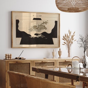 May include: A black and white print of a Japanese landscape with the text "外八大石碑" in the upper right corner. The print is framed and hanging on a white wall above a wooden cabinet with woven cane doors.