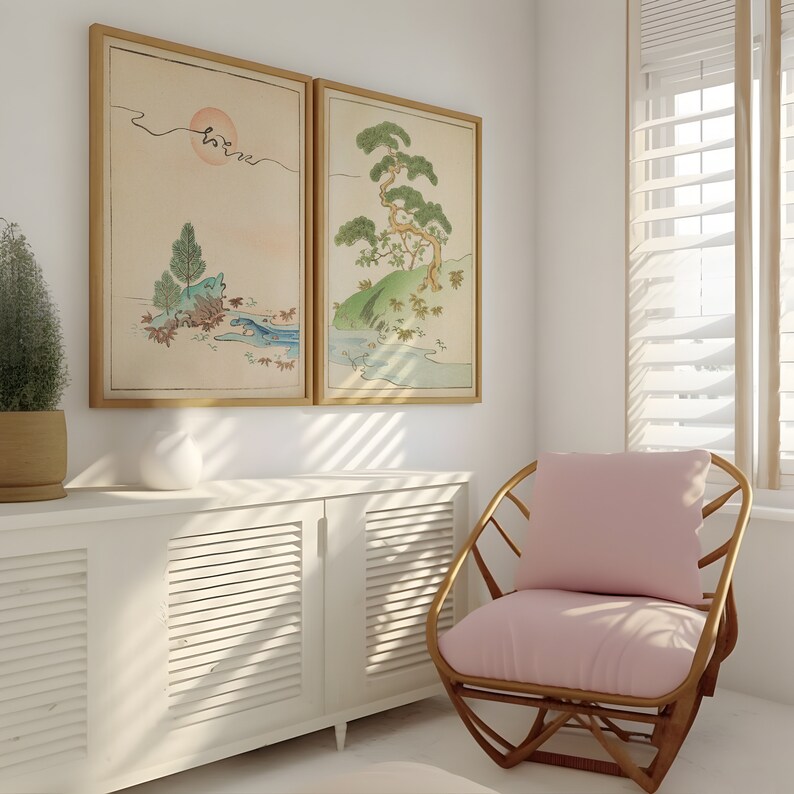 May include: Two framed prints of Japanese-style artwork depicting trees and landscapes hang on a white wall above a white cabinet with louvered doors. A pink cushioned wicker chair sits in the corner of the room.