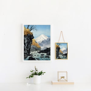 Pu&ograve; includere: Una stampa incorniciata di un paesaggio giapponese con una montagna sullo sfondo e un fiume in primo piano. La stampa &egrave; in bianco e nero e sfumature di blu e verde. La stampa &egrave; appesa a un muro bianco con un piccolo specchio dorato appeso sotto.