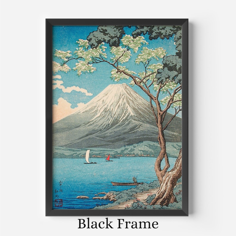 Op de afbeelding: Ingelijste kunstdruk met een Japans landschap met de berg Fuji, een meer en boten. Het kunstwerk zit in een zwarte lijst. De lucht is blauw met witte wolken en de berg is besneeuwd. Een boom met groene bladeren en witte bloemen staat op de voorgrond.