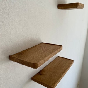 May include: Three wooden shelves mounted on a white wall. The shelves are rectangular and have rounded edges. The shelves are made of light brown wood.