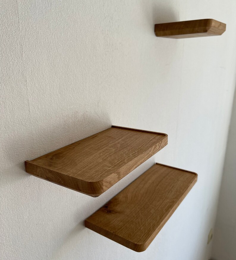 May include: Three wooden shelves mounted on a white wall. The shelves are rectangular and have rounded edges. The shelves are made of light brown wood.