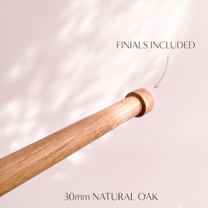 Könnte beinhalten: Eine 30mm Vorhangstange aus natürlicher Eiche mit einer zylindrischen Endkappe. Der Text FINIALS INCLUDED ist mit einem Pfeil zur Endkappe sichtbar, und der Text 30mm NATURAL OAK ist unten im Bild aufgedruckt.