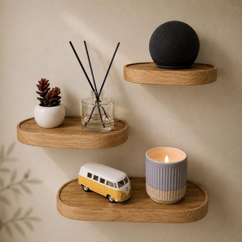 May include: Three wooden floating shelves with decorative items. A small succulent in a white pot, a glass diffuser with black reeds, a black sphere speaker, a yellow and white toy van, and a lit candle in a blue and beige ceramic holder.