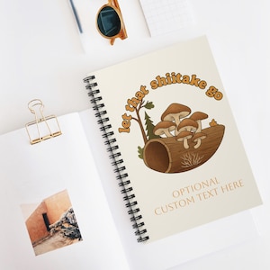 May include: Spiral-bound notebook with a cream-colored cover featuring a mushroom illustration inside a log. The text "let that shiitake go" is arched above the illustration, with the words "Optional Custom Text Here" below.