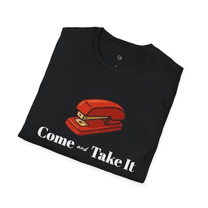 May include: Black t-shirt featuring a red stapler graphic with the text "Come and Take It" in white. The design is centered on the front of the folded shirt, offering a bold statement.