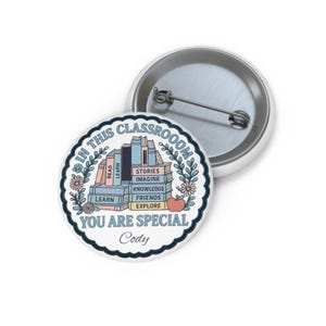 May include: A white button with a pin back, featuring a colorful design with the text "IN THIS CLASSROOM YOU ARE SPECIAL Cody". The design includes stacks of books, flowers, and an apple, with words like "LEARN" and "EXPLORE".