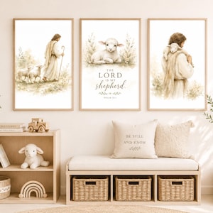 Könnte beinhalten: Drei gerahmte Wandbilder mit Aquarellillustrationen eines Hirten und Lämmern. Der mittlere Druck enthält den Text 'THE LORD IS MY shepherd' und 'PSALM 23:1'. Die Kunstwerke verwenden sanfte Beige- und Brauntöne auf weißem Hintergrund.