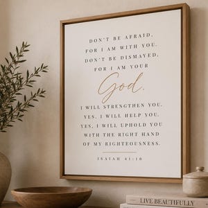 May include: A square wall art piece in a light wood frame featuring black text on a white background that reads: DON'T BE AFRAID, FOR I AM WITH YOU. DON'T BE DISMAYED, FOR I AM YOUR God. I WILL STRENGTHEN YOU. YES, I WILL HELP YOU. ISAIAH 41:10.