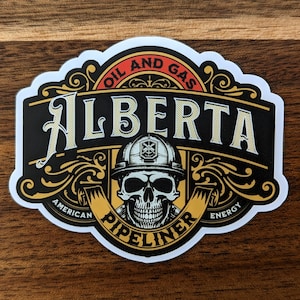 Op de afbeelding: Een witte sticker met een zwart en gouden ontwerp. De sticker toont een schedel die een helm draagt met de woorden "Oil and Gas Alberta" boven de schedel en "American Pipeliner Energy" onder de schedel.