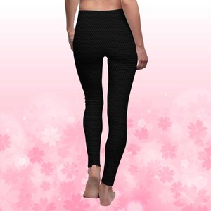 May include: Black leggings with a textured pattern. The leggings are form-fitting and reach the ankles. The background is a soft pink with a floral design.