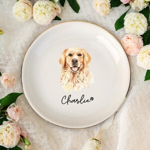 May include: White ceramic plate with a gold rim, featuring a watercolor portrait of a Golden Retriever. The dog's name, "Charlie," is written in script below the image, along with a paw print. The plate is surrounded by flowers.