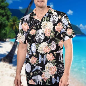 May include: A black short-sleeved button-up shirt with a floral print featuring Star Wars characters like Darth Vader, Stormtroopers, R2-D2, and a TIE fighter.