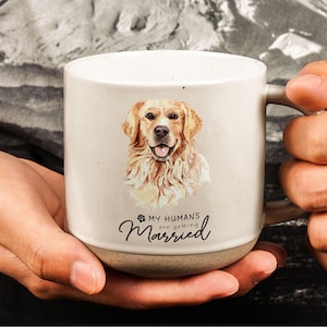May include: Cream-colored ceramic mug featuring a watercolor illustration of a Golden Retriever. The mug has the text "MY HUMANS are getting Married" in a script font. The mug has a brown base and a large handle.