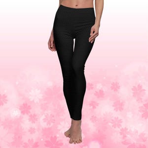May include: Black leggings with a repeating geometric pattern. The leggings are high-waisted and form-fitting, made of a stretchy material. The background is a soft pink with white floral accents.