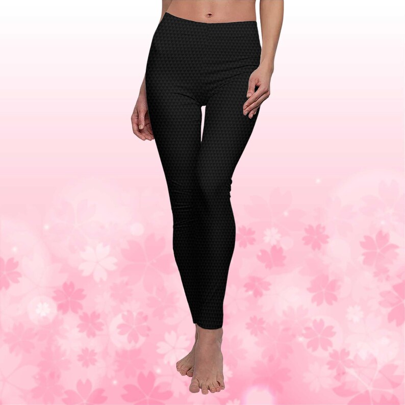 May include: Black leggings with a repeating geometric pattern. The leggings are high-waisted and form-fitting, made of a stretchy material. The background is a soft pink with white floral accents.