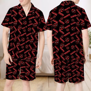 May include: Black pajama set with a repeating red Deadpool logo and text pattern. The short-sleeved shirt has a notched collar, and the shorts have an elasticated waistband. The set is made of a lightweight fabric.
