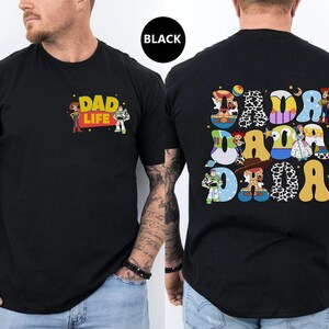 May include: Black t-shirt with a Toy Story theme. The front of the shirt says "Dad Life" with Woody and Buzz Lightyear characters. The back of the shirt has a large "Dada" spelled out with different Toy Story characters in each letter.