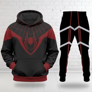Puede incluir: Conjunto de sudadera con capucha y pantal&oacute;n a juego de color negro. La sudadera con capucha presenta un dise&ntilde;o de telara&ntilde;a roja y un emblema de ara&ntilde;a en el pecho. Los pantalones son negros con detalles en rojo y blanco.