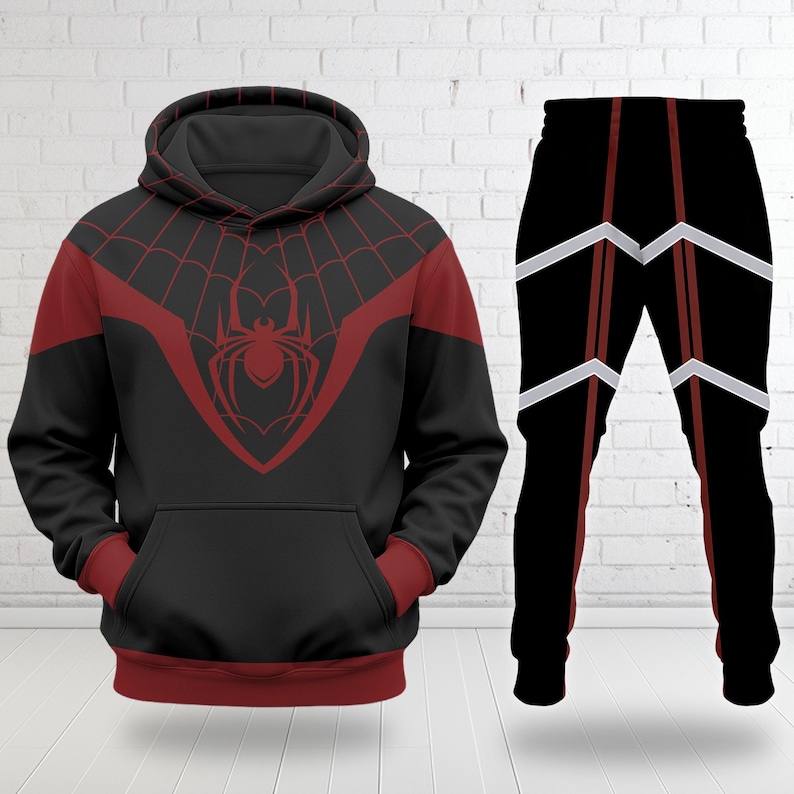 Puede incluir: Conjunto de sudadera con capucha y pantal&oacute;n a juego de color negro. La sudadera con capucha presenta un dise&ntilde;o de telara&ntilde;a roja y un emblema de ara&ntilde;a en el pecho. Los pantalones son negros con detalles en rojo y blanco.
