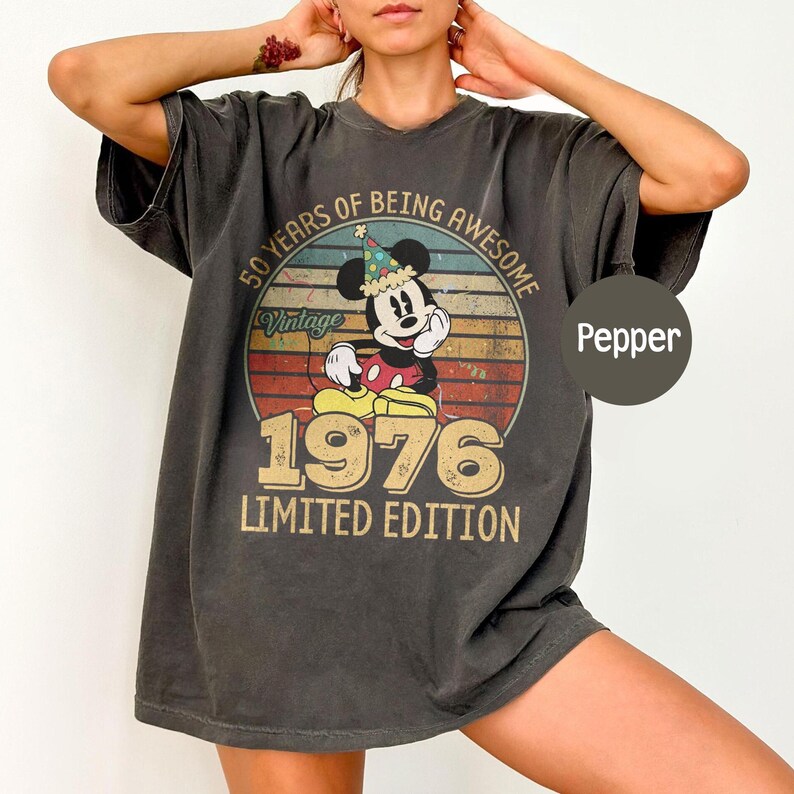 Puede incluir: Camiseta color pimienta con un dise&ntilde;o vintage de Mickey Mouse con gorro de fiesta. El gr&aacute;fico incluye el texto "50 Years of Being Awesome", "Vintage", "1976" y "Limited Edition". La camiseta tiene un corte holgado y mangas cortas.