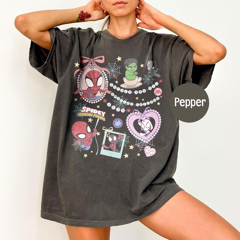 Puede incluir: Camiseta de gran tama&ntilde;o color pimienta con ilustraciones de dibujos animados de Spider-Man y sus amigos. El dise&ntilde;o incluye un gr&aacute;fico en forma de coraz&oacute;n, telara&ntilde;as y el texto "Spidey Amazing Friends".