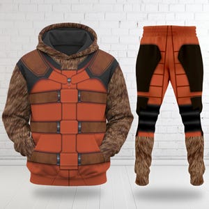 Peut inclure: Un ensemble sweat à capuche et pantalon orange et marron. Le sweat à capuche présente une capuche et des manches en fausse fourrure, avec un design ressemblant à une armure. Le pantalon a un design similaire avec de la fausse fourrure aux chevilles.