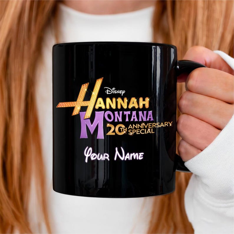 Puede incluir: Taza de cer&aacute;mica negra con el logotipo de Hannah Montana 20th Anniversary Special en dorado, morado y blanco. La taza incluye el logotipo de Disney y espacio para un nombre personalizado en escritura blanca. Una taza de caf&eacute; cl&aacute;sica.