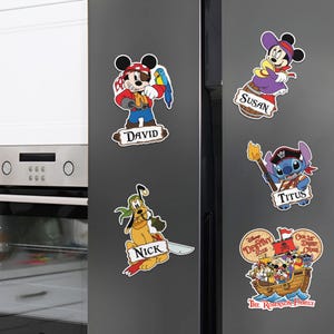Op de afbeelding: Een verzameling kleurrijke Disney piratenmagneten. Met Mickey Mouse, Minnie Mouse, Pluto en Stitch, elke magneet heeft een naam erop. Een piratenschipmagneet heeft de tekst "Disney Destiny 2025" en "Our 1st Disney Cruise".