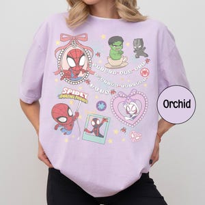 Puede incluir: Camiseta color orqu&iacute;dea con ilustraciones de dibujos animados de Spider-Man, Spider-Gwen, Hulk y Pantera Negra. La camiseta incluye el texto "Spidey Amazing Friends" y otros elementos decorativos.