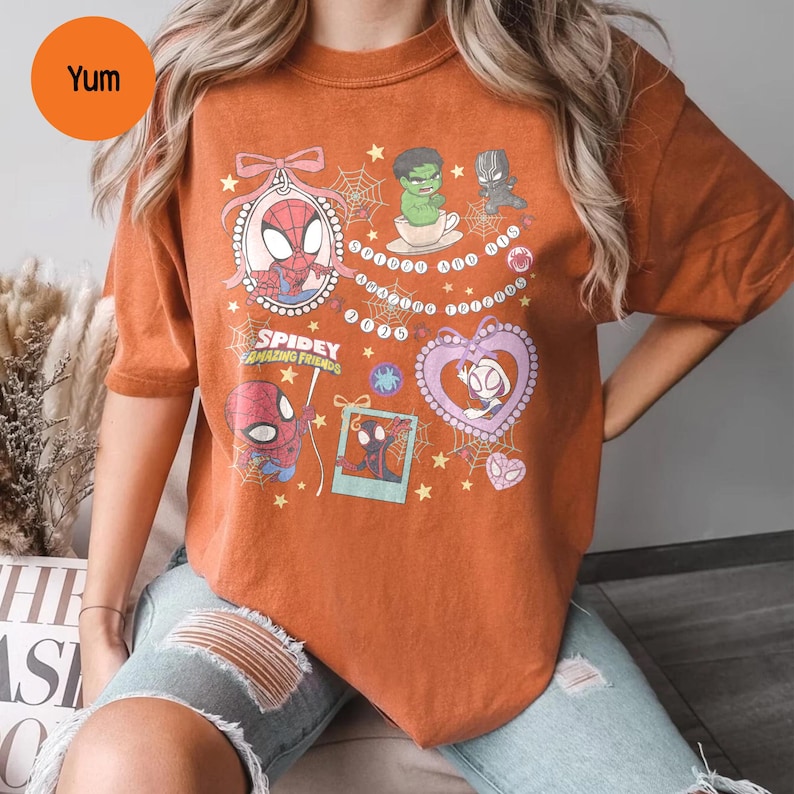 Puede incluir: Camiseta naranja quemado con un dise&ntilde;o que presenta personajes de Spider-Man y el texto "Spidey Amazing Friends". El dise&ntilde;o incluye a Spider-Man, Spider-Gwen, Hulk y Black Panther, con telara&ntilde;as y estrellas. La palabra "Yum" est&aacute; en un c&iacute;rculo en la parte superior izquierda.