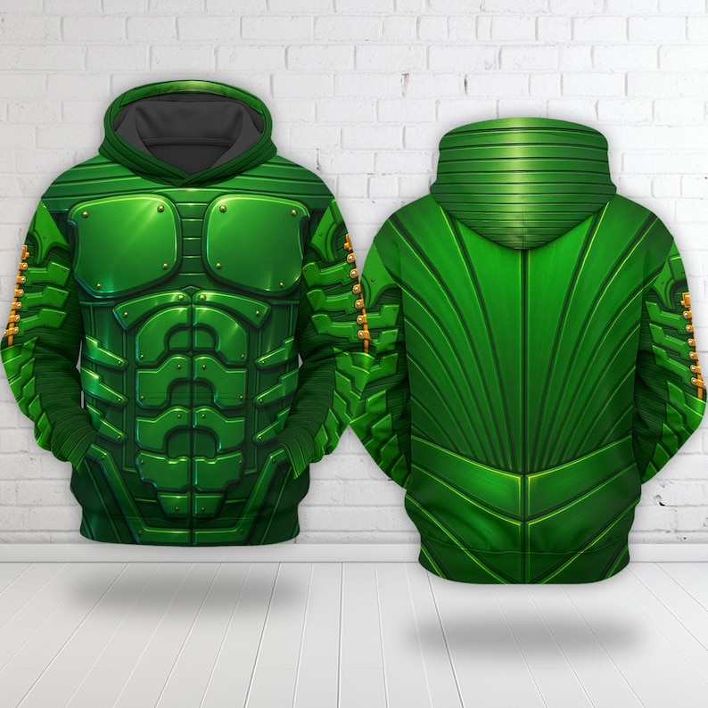 K&ouml;nnte beinhalten: Zwei gr&uuml;ne Kapuzenpullover mit einem detaillierten Design, das einer R&uuml;stung &auml;hnelt. Die Vorderseite des Kapuzenpullovers weist ein Brustplatten-Design mit metallischen Akzenten auf. Die R&uuml;ckseite des Kapuzenpullovers hat ein geripptes Muster. Die Kapuzenpullover werden vor einer wei&szlig;en Backsteinmauer pr&auml;sentiert.