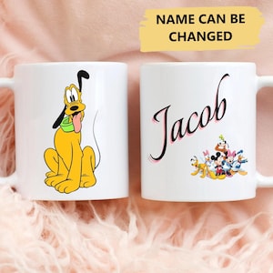 May include: Two white ceramic mugs. One mug features a cartoon image of Pluto, a yellow dog with a green collar. The other mug has the name "Jacob" written in pink cursive and a group of cartoon Disney characters. The text "NAME CAN BE CHANGED" is written in yellow on a white background.