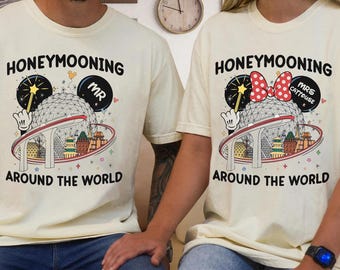 May include: A couple's matching t-shirts with a light beige background. The shirts feature a cartoon image of Mickey Mouse and Minnie Mouse with the text "Honeymooning Around the World". The shirts also include the text "Mr." and "Mrs. Catmouse".