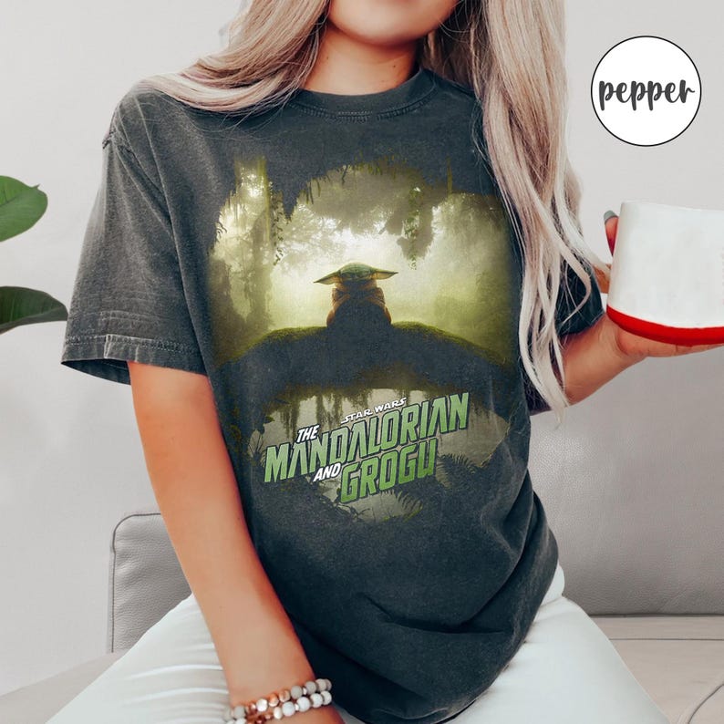 May include: Dark gray t-shirt featuring a graphic of Grogu from The Mandalorian series. The image shows Grogu in a forest setting, with the text "Star Wars The Mandalorian and Grogu" in green and white.