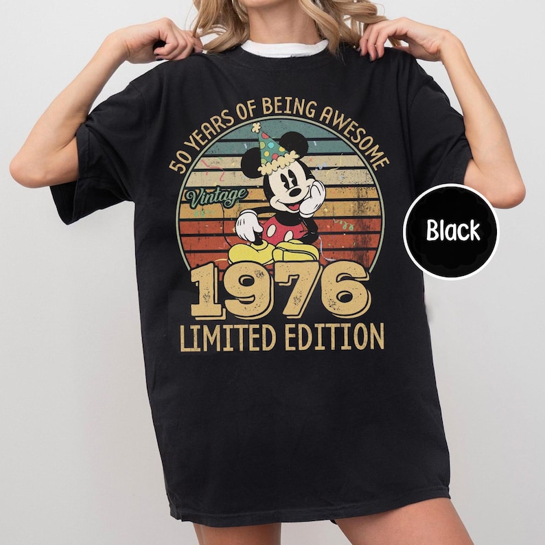 Puede incluir: Camiseta negra con un dise&ntilde;o vintage de Mickey Mouse con un gorro de fiesta. El dise&ntilde;o incluye el texto "50 Years of Being Awesome" y "1976 Limited Edition". La camiseta tiene un estilo retro.