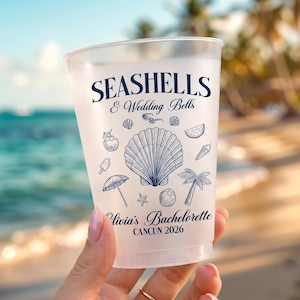 May include: A frosted plastic cup featuring dark blue text that reads SEASHELLS & Wedding Bells, Olivia's Bachelorette, and CANCUN 2026. The cup is decorated with line art illustrations of a large seashell, palm tree, umbrella, and beach items.
