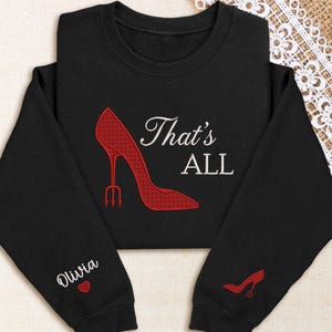 May include: Black sweatshirt with a red high heel shoe design and the text "That's ALL" in white. The left sleeve has the name "Olivia" and a heart. The right sleeve has a small red high heel shoe.