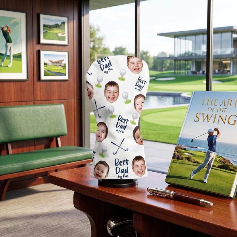Puede incluir: Una funda blanca para la cabeza del palo de golf con un patr&oacute;n repetido de caras de ni&ntilde;os sonrientes, pelotas de golf y palos de golf cruzados. El texto "Best Dad by Par" tambi&eacute;n est&aacute; impreso en la funda. Un libro titulado "The Art of the Swing" es visible.