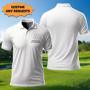 Peut inclure: Polo blanc avec un motif en nid d'abeille et un design sur le th&egrave;me du golf. Le t-shirt pr&eacute;sente un graphique de clubs de golf et le texte "BEST GRANDPA BY PAR". Le t-shirt a un col classique et des manches courtes. L'image montre &eacute;galement le dos du t-shirt.