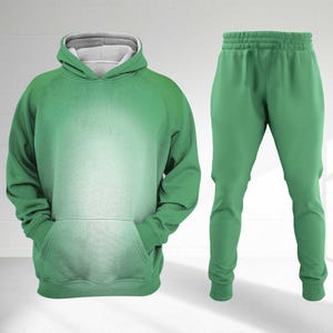 May include: A green tracksuit comprising a hoodie and matching trousers. The hoodie features a grey-lined hood and a front pocket. The trousers have an elasticated waistband and ankle cuffs. The set is a solid green colour.