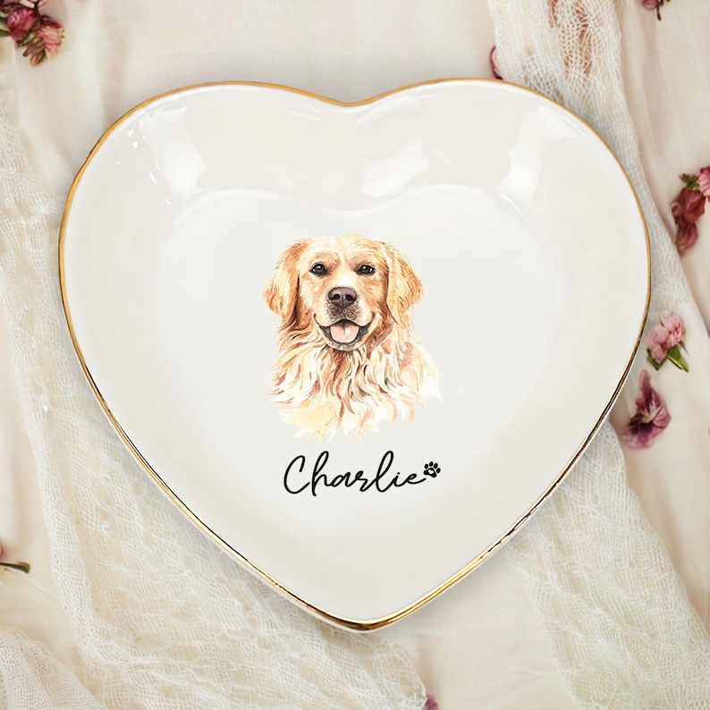 May include: Heart-shaped white ceramic dish with a gold rim. The dish features a watercolor portrait of a Golden Retriever dog. The dog's name, "Charlie," is written in script below the image, along with a paw print.